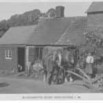 Sepia postcard showing men, horses and plough outside blacksmith's shop Brighstone, IW