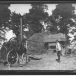 Photographic print taken from a glass plate negative in the collection of men working a threshing machine driven by a steam engine