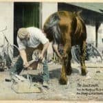 Tinted photograph shows a blacksmith shoeing a horse, with tools and a bicycle visible in the background