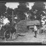 Photographic print taken from a glass plate negative in the collection of men working a threshing machine driven by a steam engine