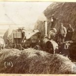 A sepia photograph showing good detail of a threshing machine, crew and steam engine